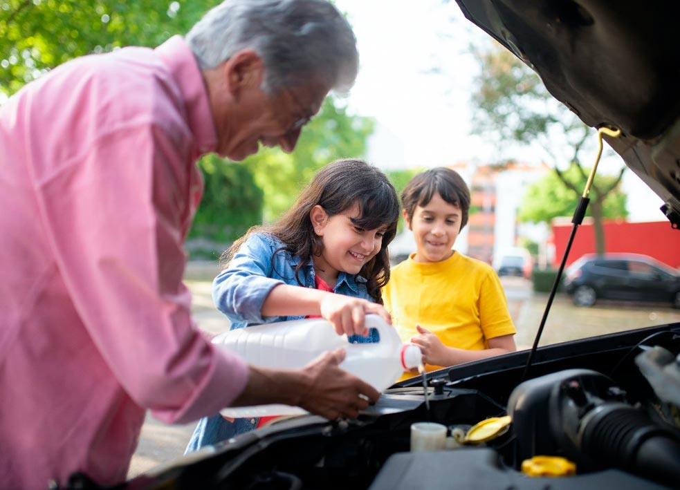 Unos niños disfrutan de la experiencia de viajar en autocaravana ayudando a su abuelo con el mantenimiento del vehículo.